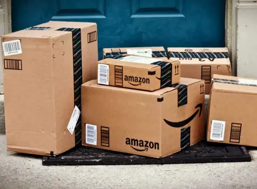 A collection of Amazon packages stacked on a doorstep, representing the outcomes of refund-for-review and online side hustle programs.